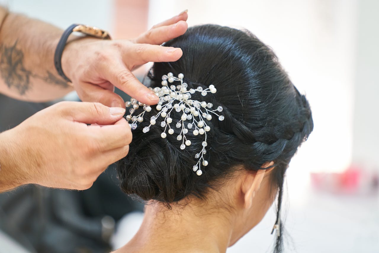 about-me-02 Photograph of a hairstylist arranging an elegant updo embellished with delicate decorative pins in a professional studio.